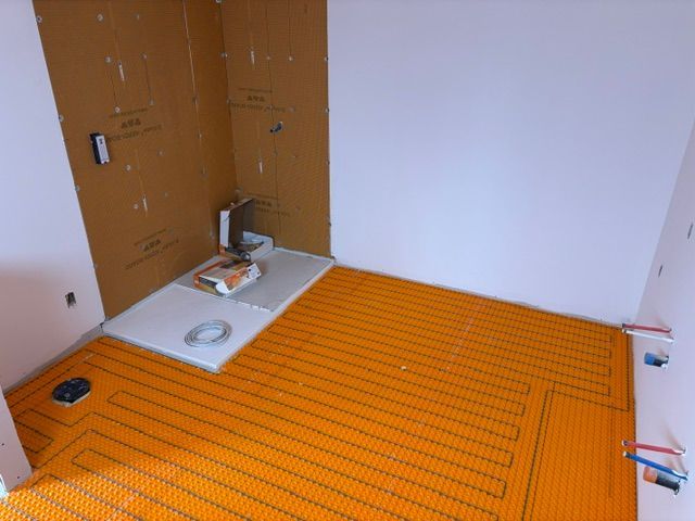 Salle de bains en construction, chauffage au sol orange, panneaux muraux marron, murs blancs.