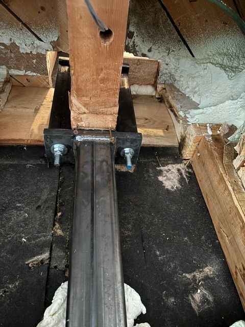 Poteau métallique soutenu par une poutre en bois et fixé par des boulons. Installé dans un grenier.