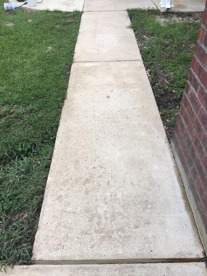 A concrete sidewalk next to a brick building and grass.