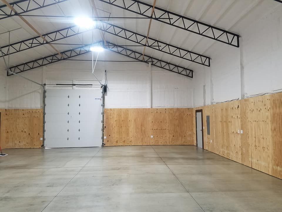 A large empty warehouse with a white garage door and wooden walls.