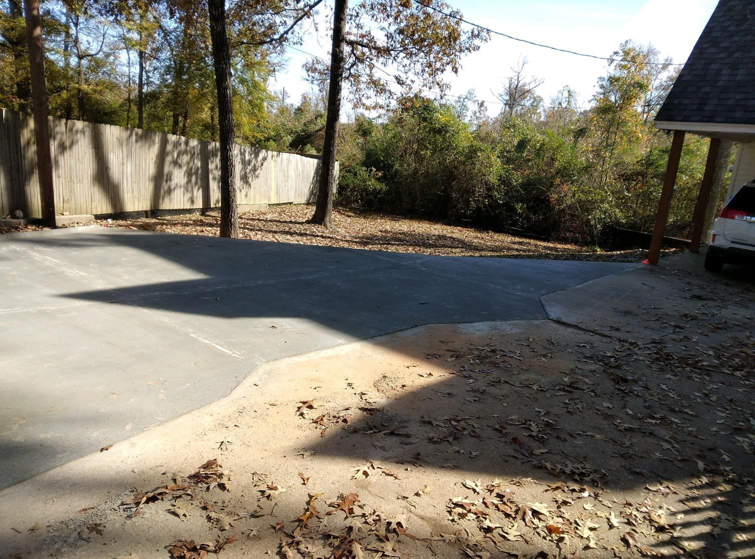 A white car is parked in a driveway next to a fence