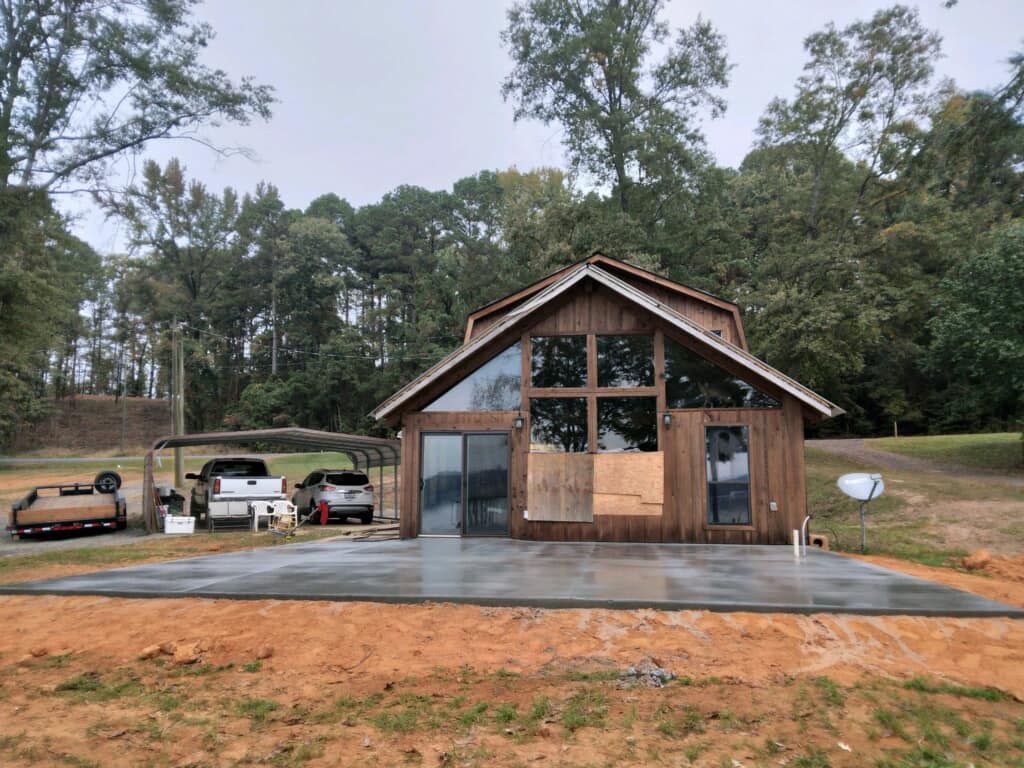 A small house with a lot of windows is sitting in the middle of a field.