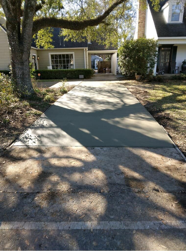 A concrete driveway leading to a house with a tree in the background.