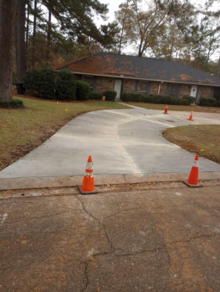 A concrete driveway with orange traffic cones in front of a house