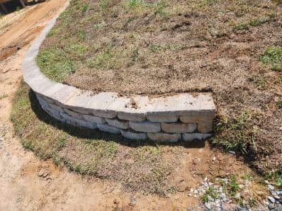 A stone wall is sitting on top of a grassy hill next to a dirt road.