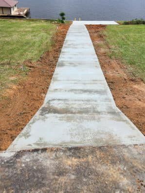 A concrete walkway leading to a lake with a house in the background.