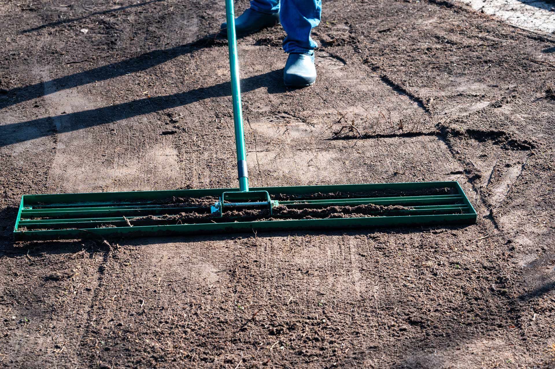 A person is using a green mop to spread dirt on the ground