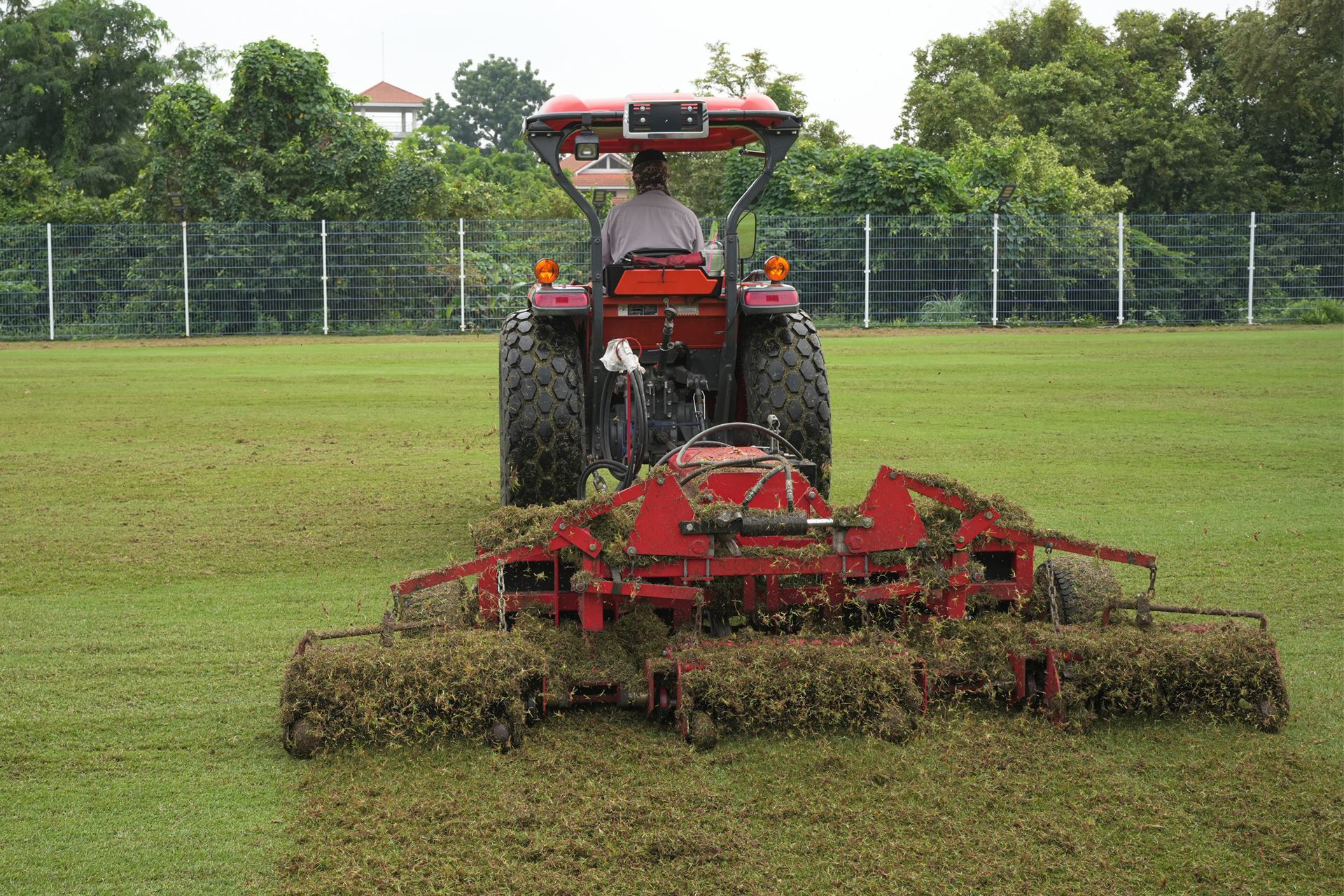 A man is driving a red tractor on a lush green field