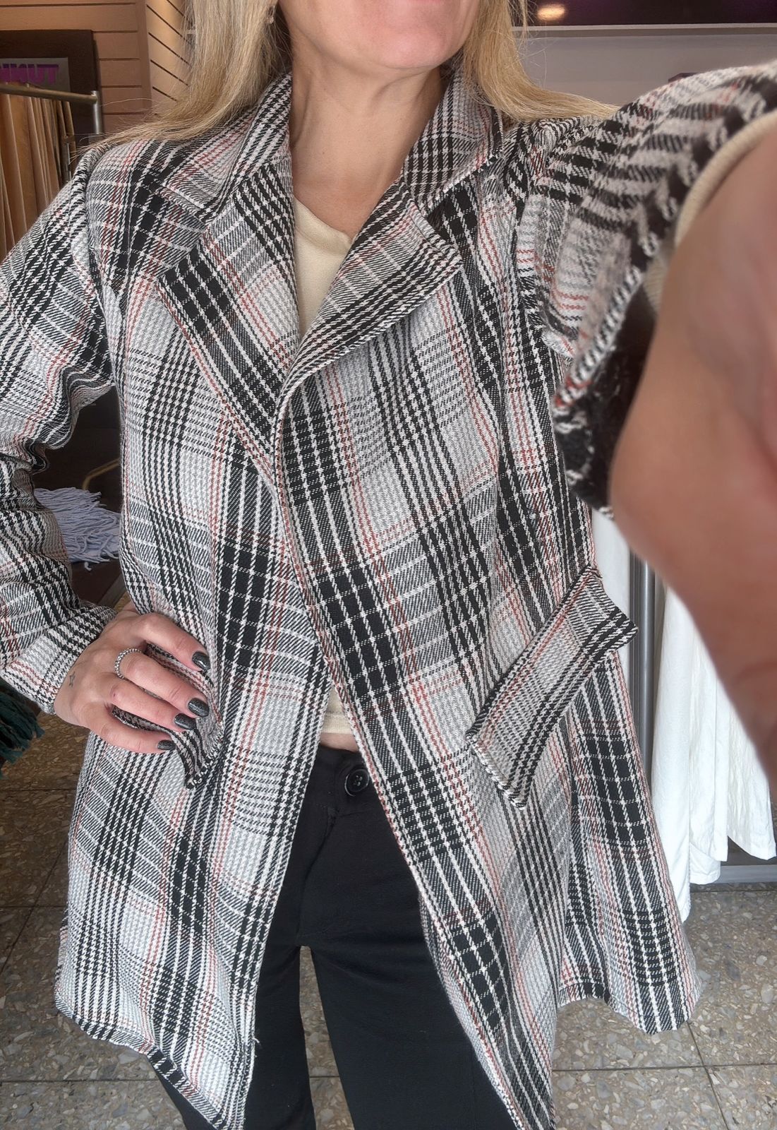 Mujer con chaqueta a cuadros posa en el interior, sonriendo, con la mano en la cadera.