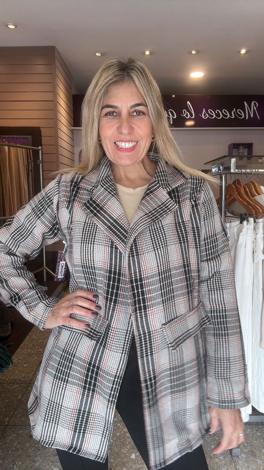 Mujer con chaqueta a cuadros posa en el interior, sonriendo, con la mano en la cadera.