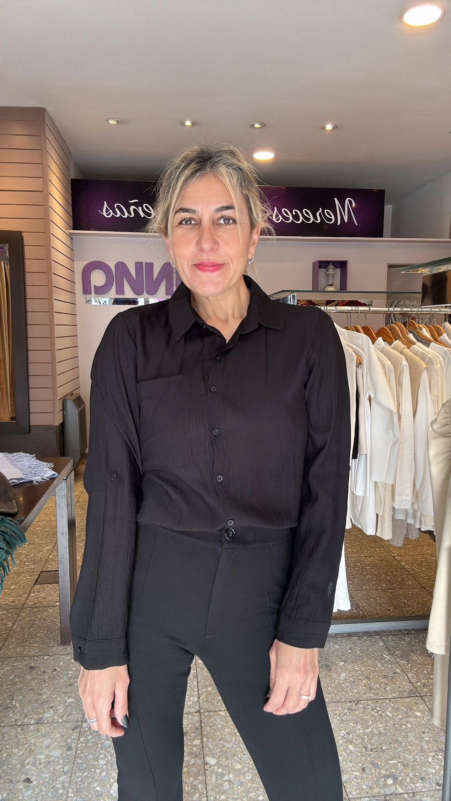 Mujer vestida de negro posa en una tienda de ropa.