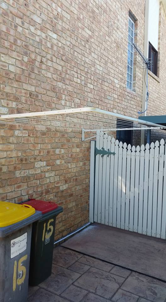 A Brick Wall With a White Picket Fence and Trash Cans in Front of It — South Coast Clothes Lines in Gerringong, NSW