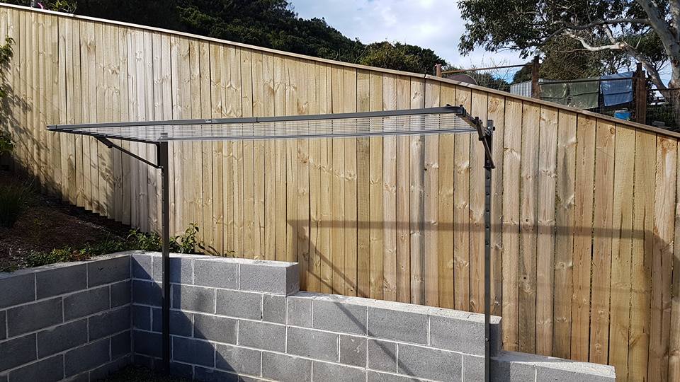 A Clothes Line is Sitting in Front of a Wooden Fence — South Coast Clothes Lines in Gerringong, NSW