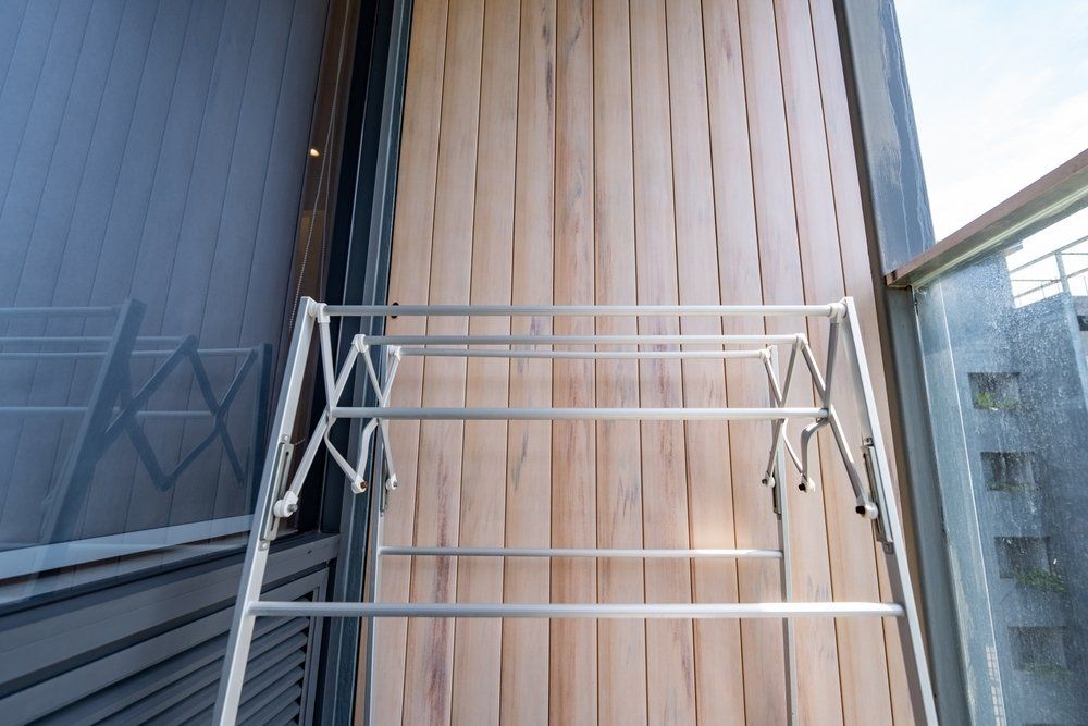 A Clothes Drying Rack is Sitting on a Balcony Next to a Window — South Coast Clothes Lines in Gerringong, NSW