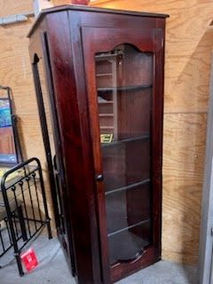 A wooden cabinet with a glass door is sitting in a room next to a bed.