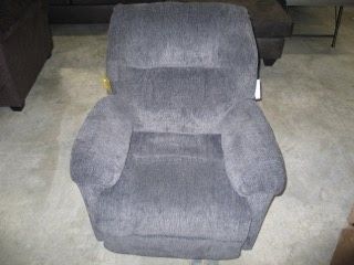 A grey recliner is sitting on a carpeted floor in a living room.