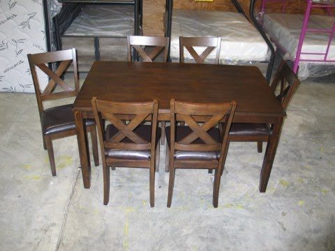 A wooden dining table with four chairs in a room with bunk beds.