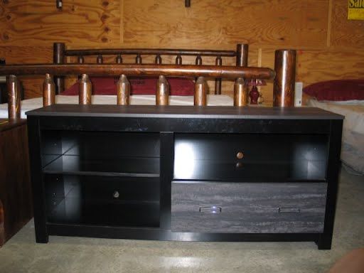 A black entertainment center is sitting in front of a wooden bed.