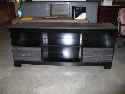 A black entertainment center is sitting on a concrete floor.
