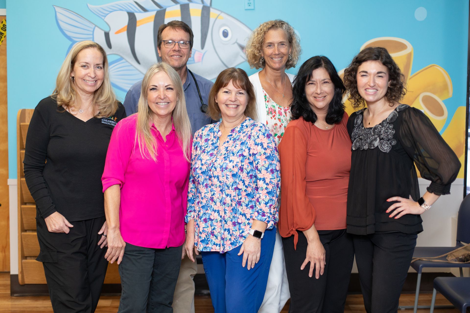 A group of people are posing for a picture in front of a mural of a fish.