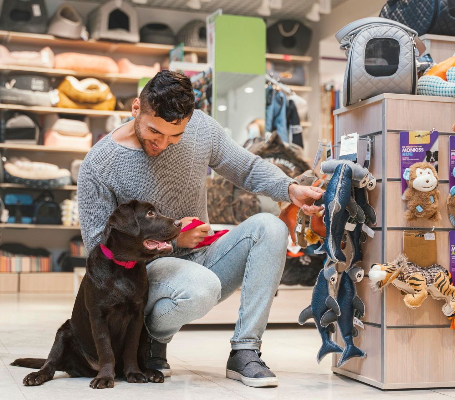 A man is kneeling down next to a dog in a pet store.