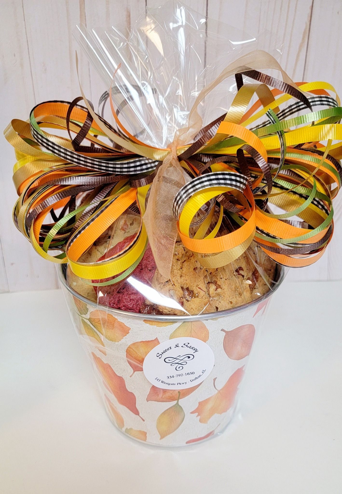 Gift basket in a leaf-patterned bucket, tied with a fall-themed bow.