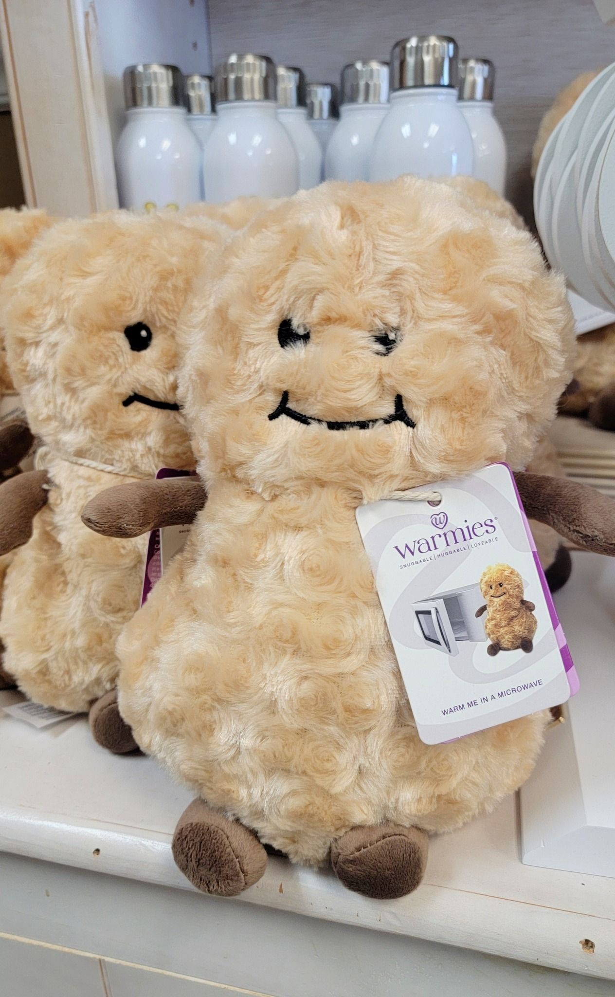 Two plush, brown mushroom-shaped toys with smiling faces and price tags on a shelf, with water bottles in the background.