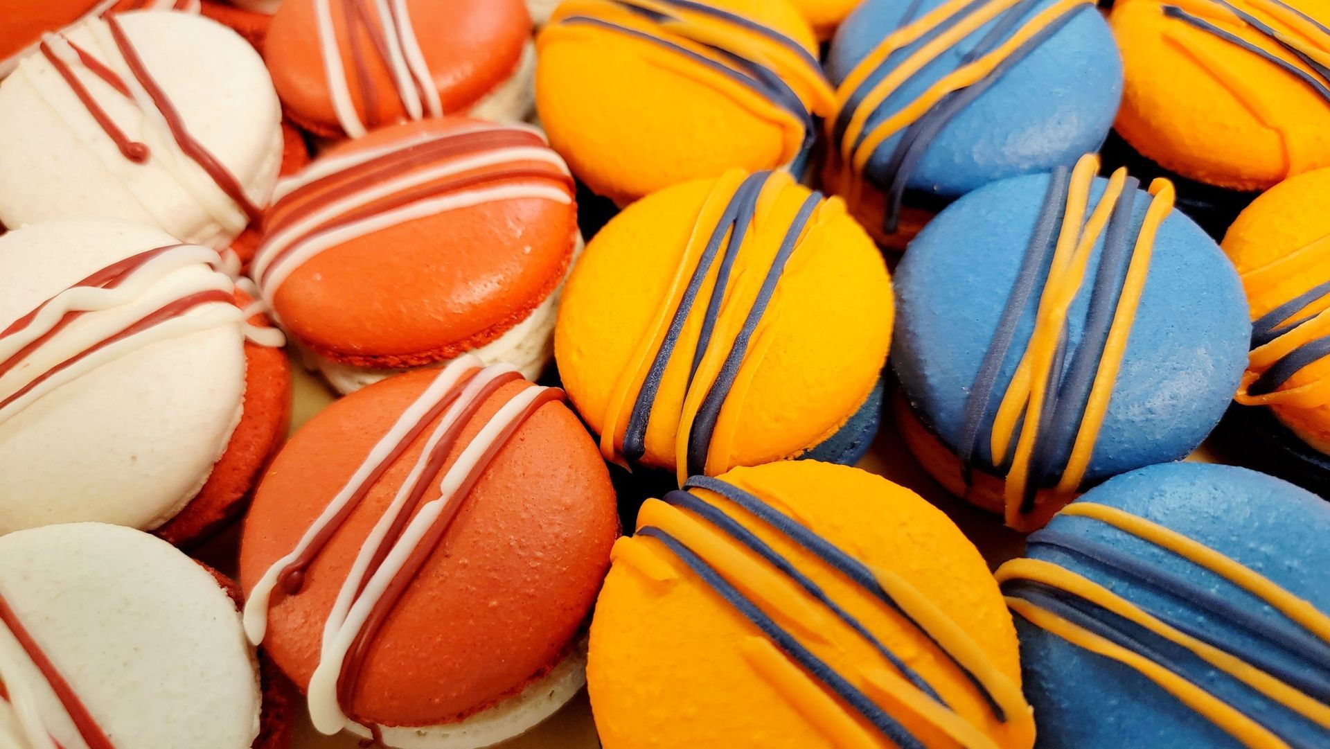 Close-up of colorful macarons: white with red stripes, red, yellow, and blue with dark stripes.