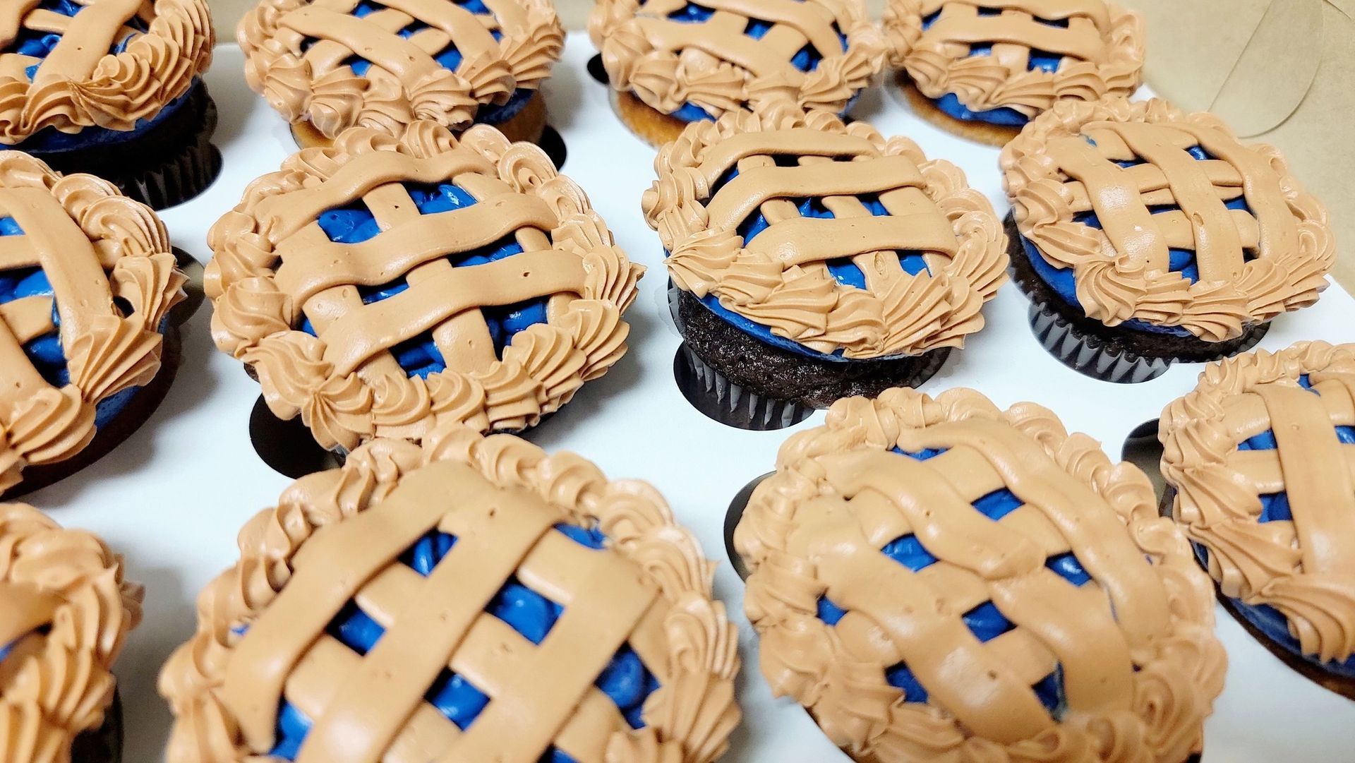 Cupcakes resembling mini blueberry pies, with lattice crust design and blue filling, arranged on a tray.