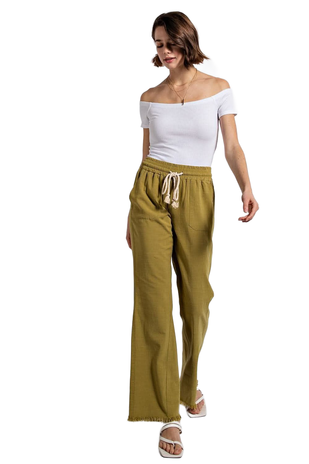 Woman in white off-the-shoulder top and olive pants with sandals walking toward the viewer.