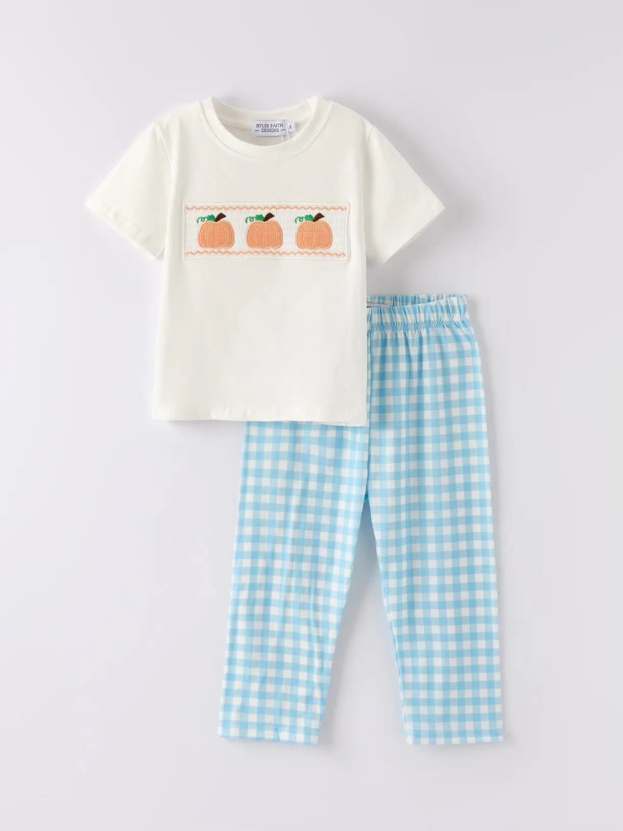 Cream-colored t-shirt with orange embroidery and blue gingham pajama pants on a white background.