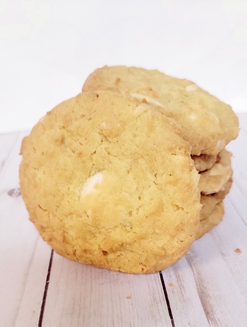 Stack of golden cookies with white chocolate chips on a white wood surface.
