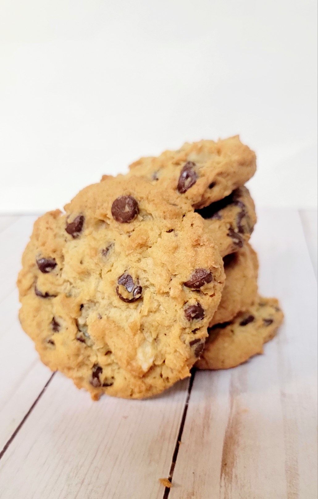 Stack of chocolate chip cookies on a light wooden surface.