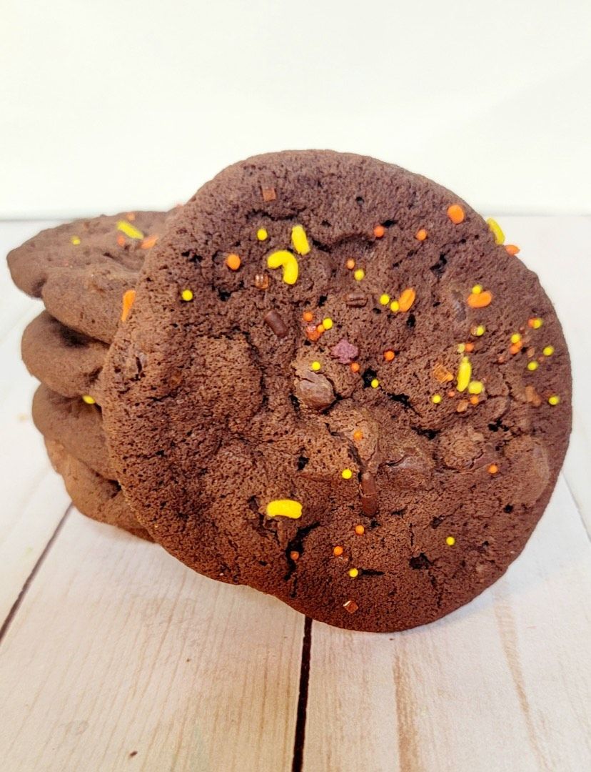 Chocolate cookies with orange and yellow sprinkles, stacked on a wooden surface.