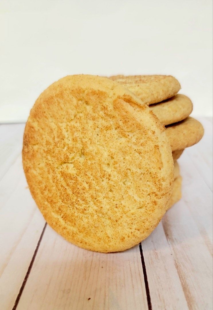 Stack of round, golden-brown snickerdoodle cookies on a light wooden surface.
