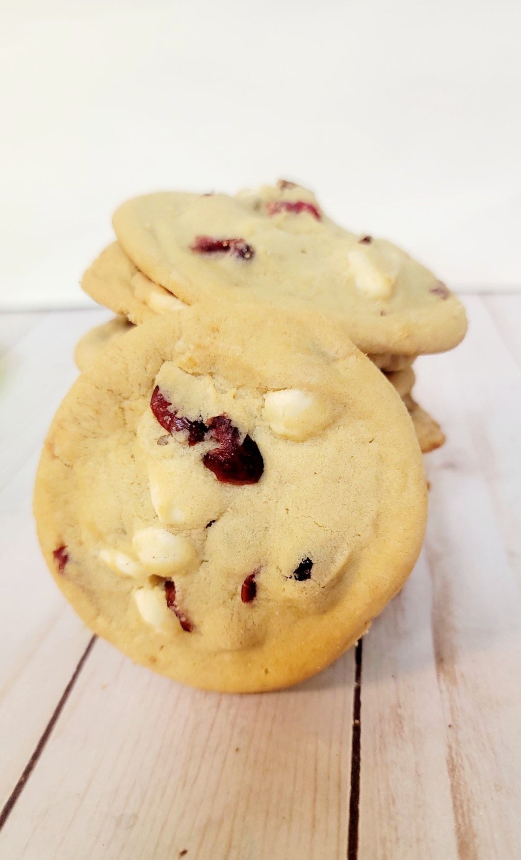 Stack of cranberry white chocolate chip cookies on a light wooden surface.