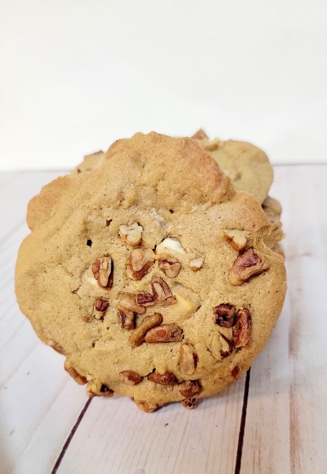 Pecan cookies on a light wood surface, stacked slightly with a white background.