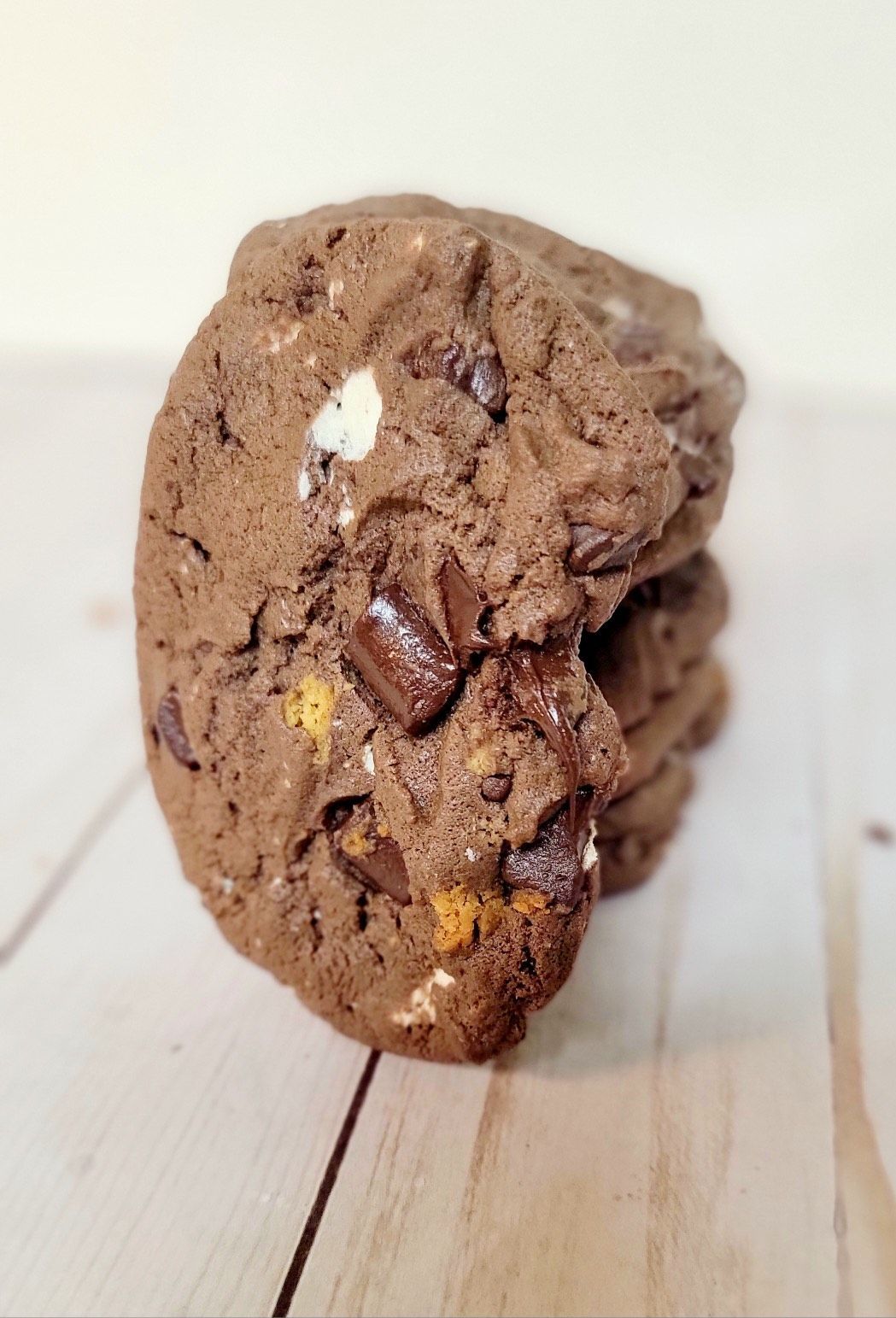 Stack of chocolate cookies with marshmallows and chocolate chunks on a wood surface.
