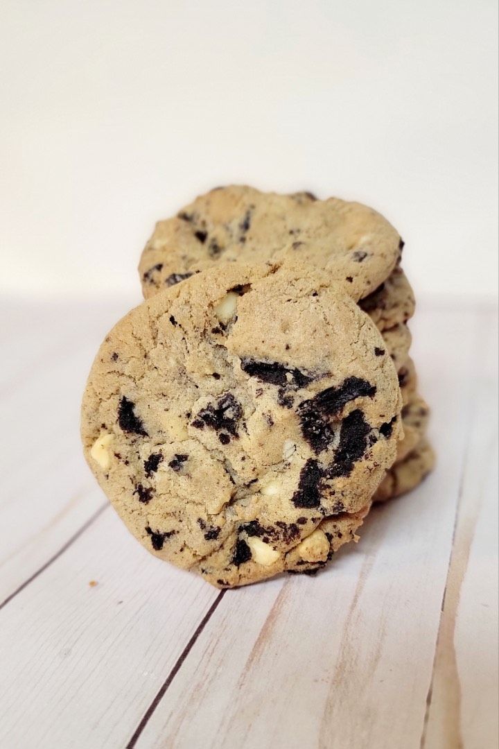 Stack of cookies with dark and white chocolate chips on a wooden surface.