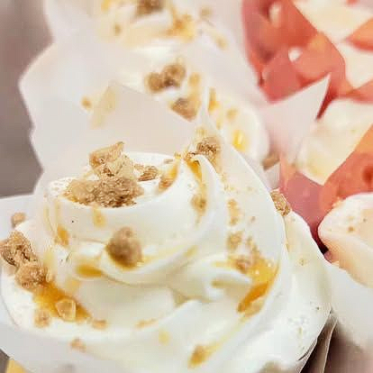 Cupcakes with white frosting, caramel drizzle, and crumbs in white paper liners.