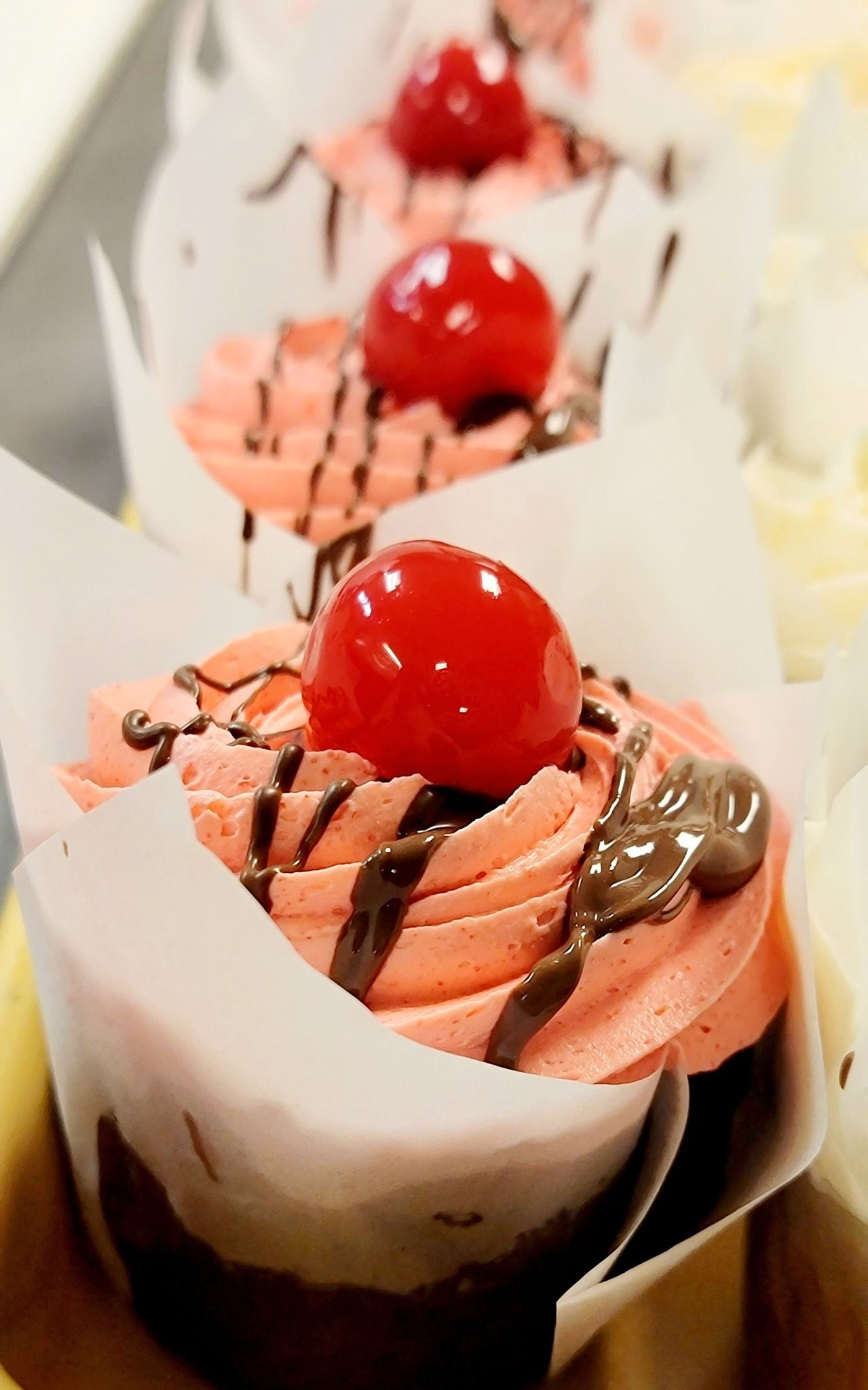 Cupcakes with pink frosting, chocolate drizzle, and a cherry on top.
