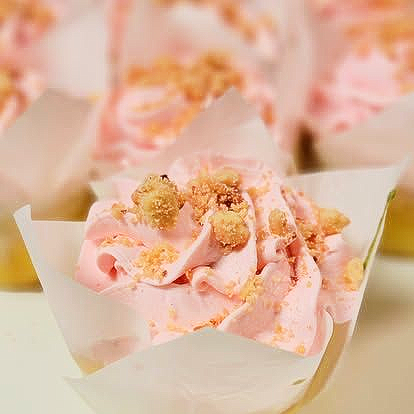 Pink frosted cupcake with crumbled topping in a white paper liner.