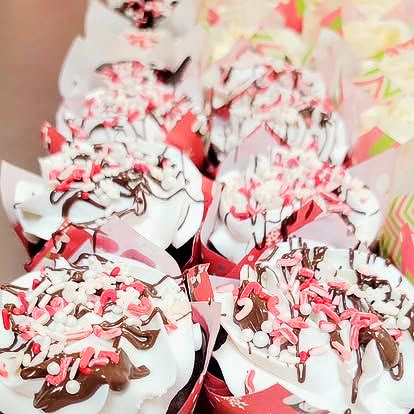 Cupcakes with white frosting, chocolate drizzle, and sprinkles in red and white wrappers.