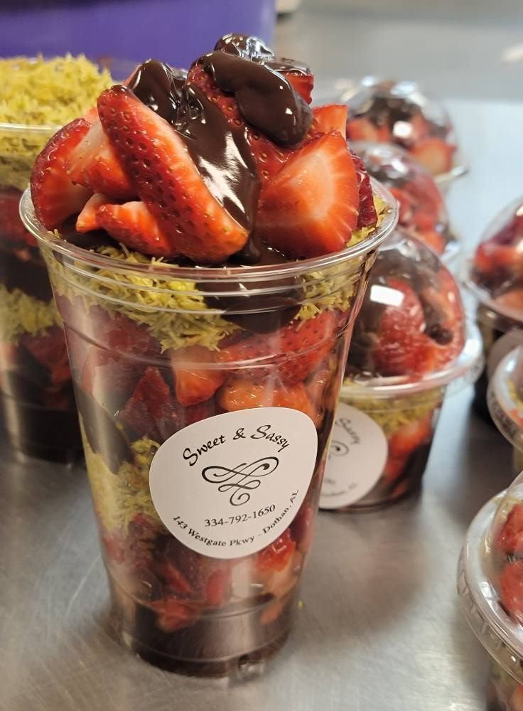 Strawberry parfait in a clear cup with green sprinkles and chocolate drizzle.