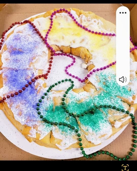 King Cake decorated with purple, green, and yellow sugar, with matching beads.