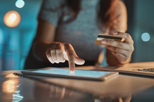 a woman is holding a credit card and using a tablet computer .