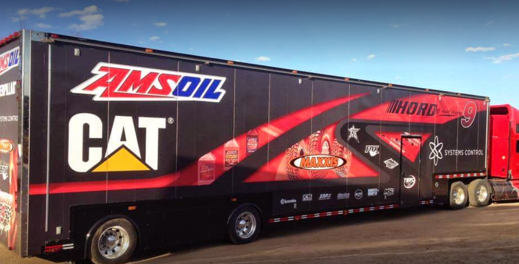 a red and black amsoil cat trailer is parked in a parking lot