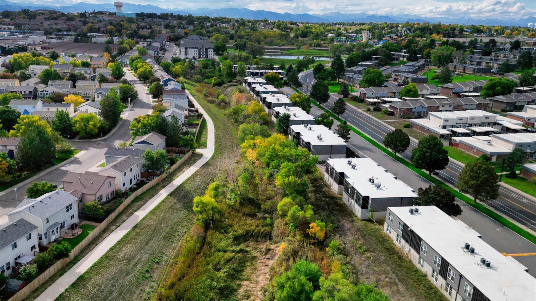 Aerial view of residential neighborhood with modern townhomes and a park. Green trees and blue sky.