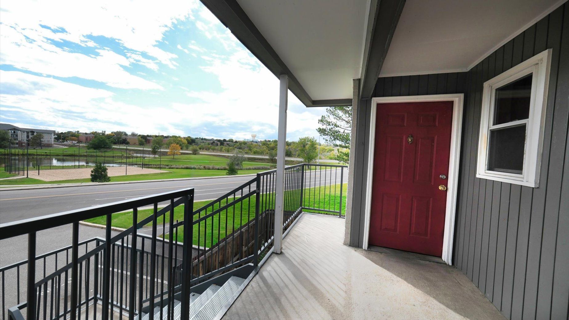 Exterior entry to a multifamily building: red door, gray siding, railing, and stairs.