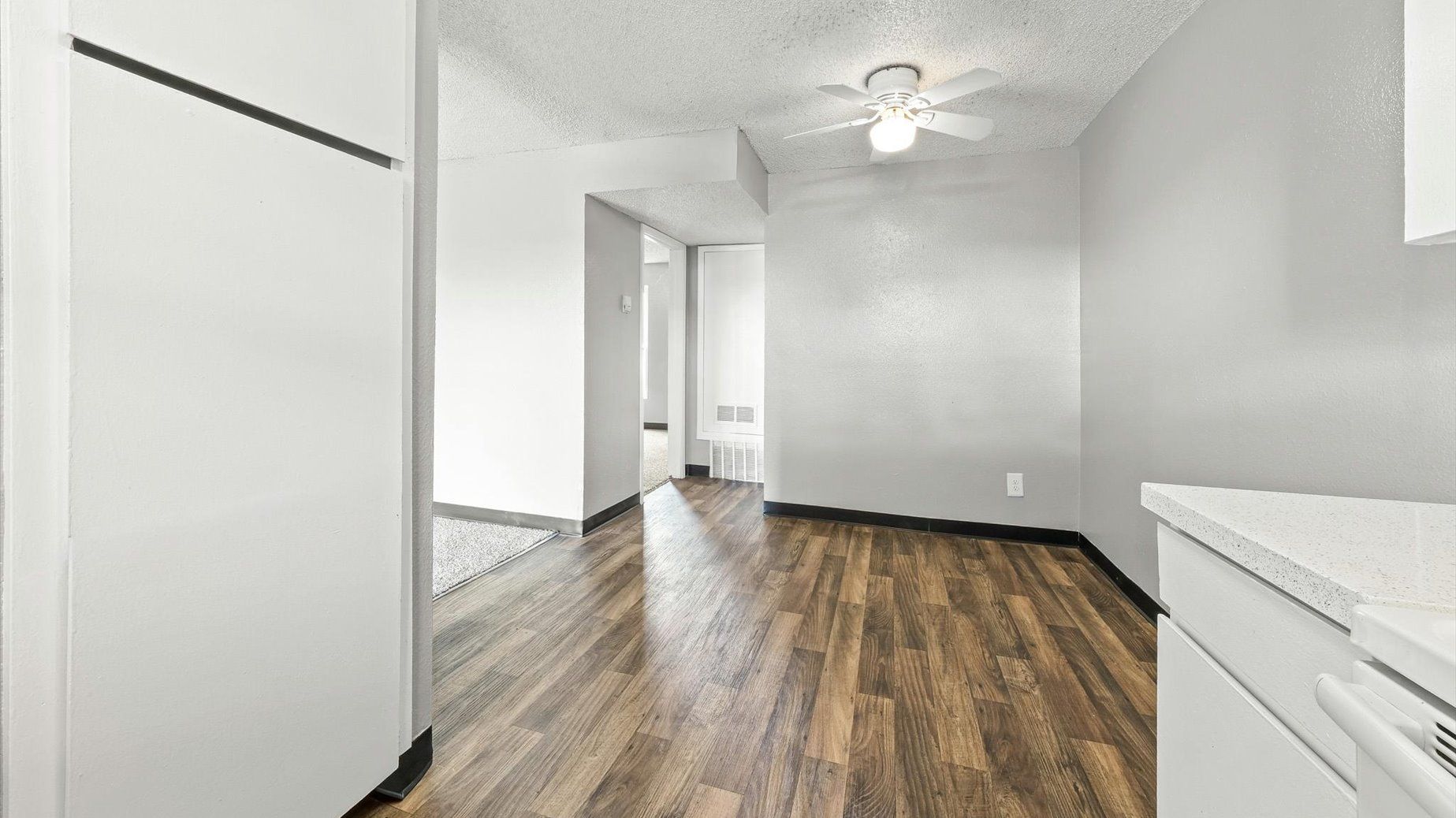 Interior of an apartment living area with wood-look flooring, white walls, and a ceiling fan.